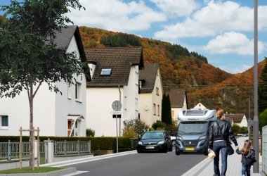 Visualisierung der fertiggestellten Straße Hohenrhein in Lahnstein: In der Mitte des Bildes die Straße unter blauem Himmel, auf der ein Wohnmobil fährt, links Häuser und rechts Fußgänger