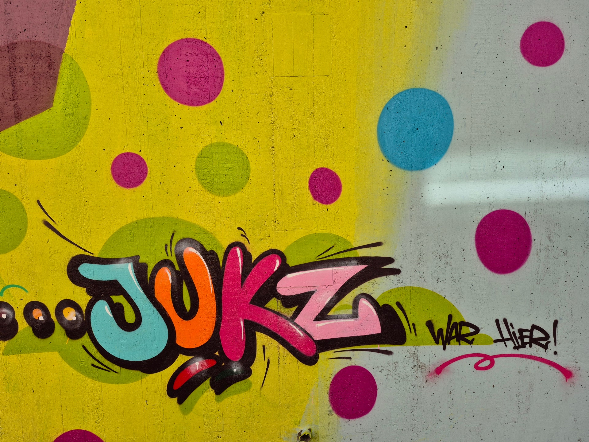 Farbfreudiges Graffiti-Kunstwerk mit dem stilisierten Schriftzug „JUKZ“ auf einem gelb-grün gepunkteten Hintergrund.