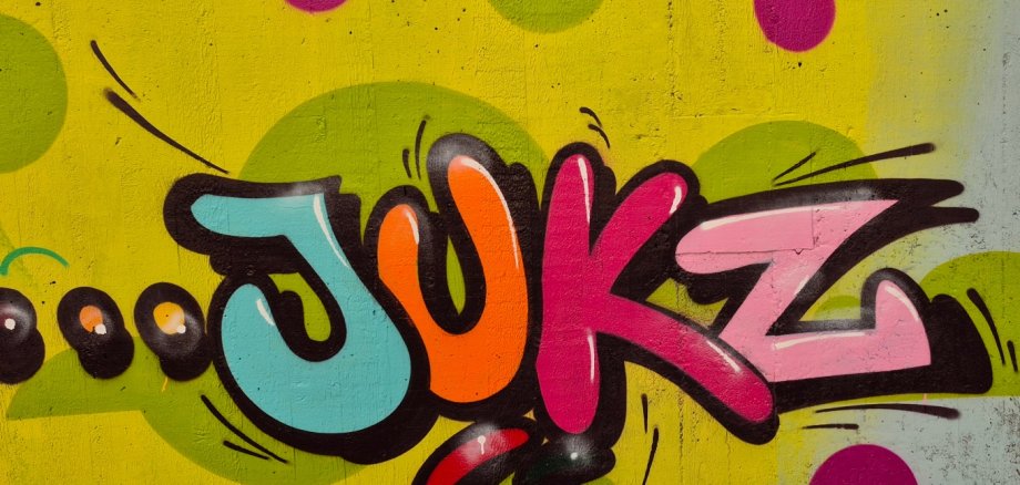 Farbfreudiges Graffiti-Kunstwerk mit dem stilisierten Schriftzug „JUKZ“ auf einem gelb-grün gepunkteten Hintergrund.