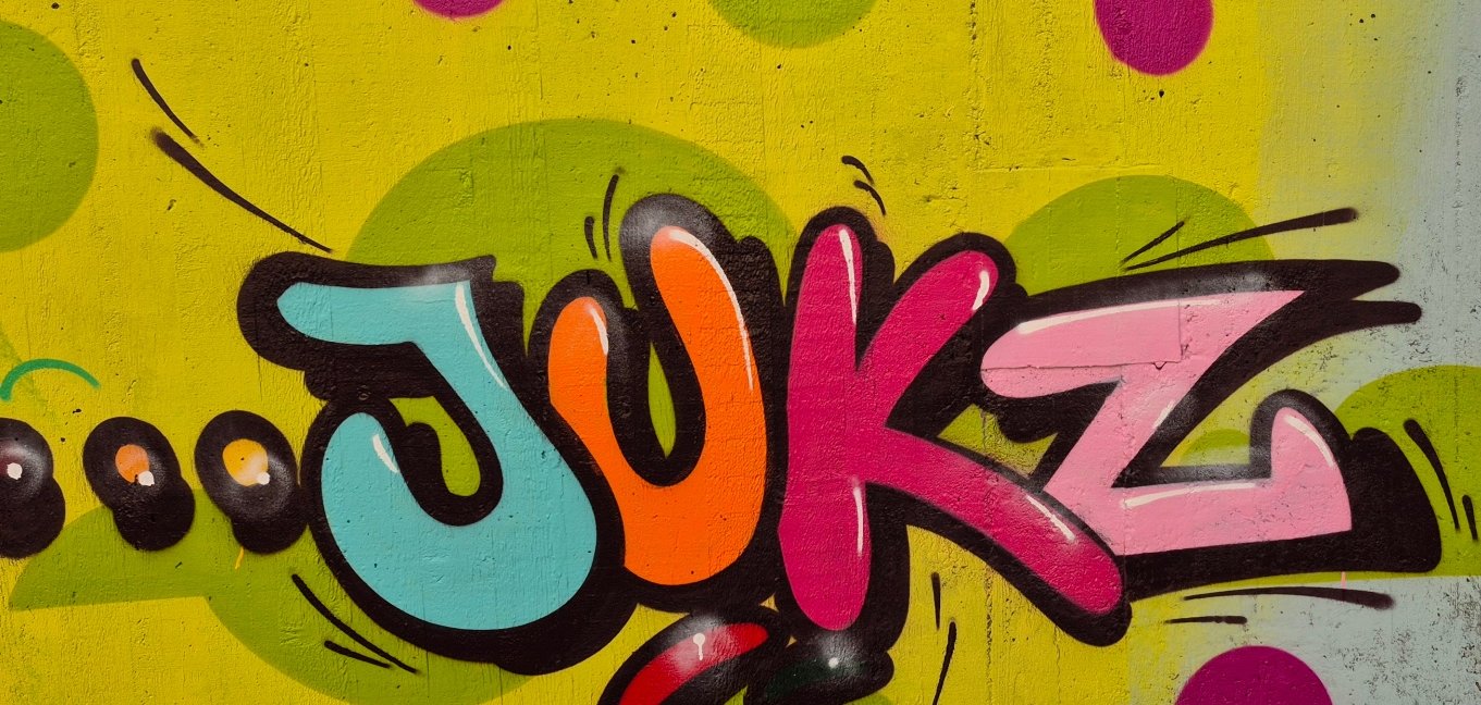 Farbfreudiges Graffiti-Kunstwerk mit dem stilisierten Schriftzug „JUKZ“ auf einem gelb-grün gepunkteten Hintergrund.