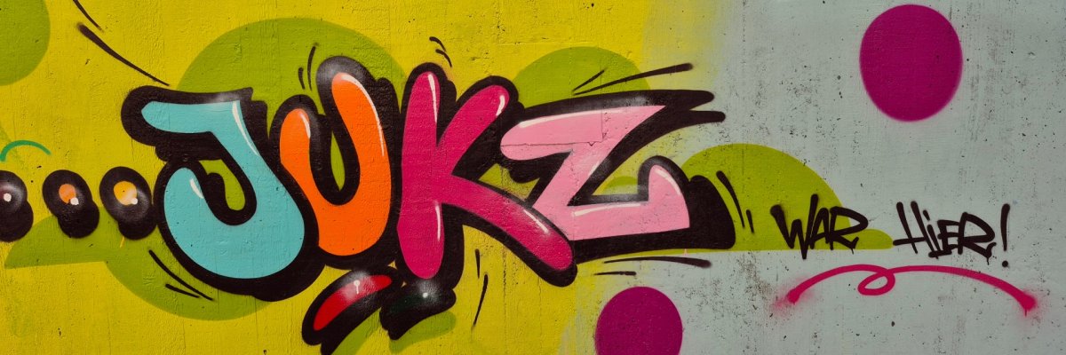 Grafitti JUKZ Farbfreudiges Graffiti-Kunstwerk mit dem stilisierten Schriftzug „JUKZ“ auf einem gelb-grün gepunkteten Hintergrund.
