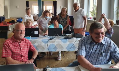 zwei Frauen und zwei Männer sitzen an Laptops im JUKZ, andere stehen hinter ihnen, alle lachen