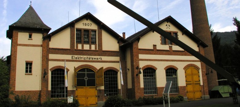 Gebäude des historischen Wasserkraftwerks vor blauem Himmel. Aufschrift 1907 und Elektrizitätswerk über der Eingangstür.