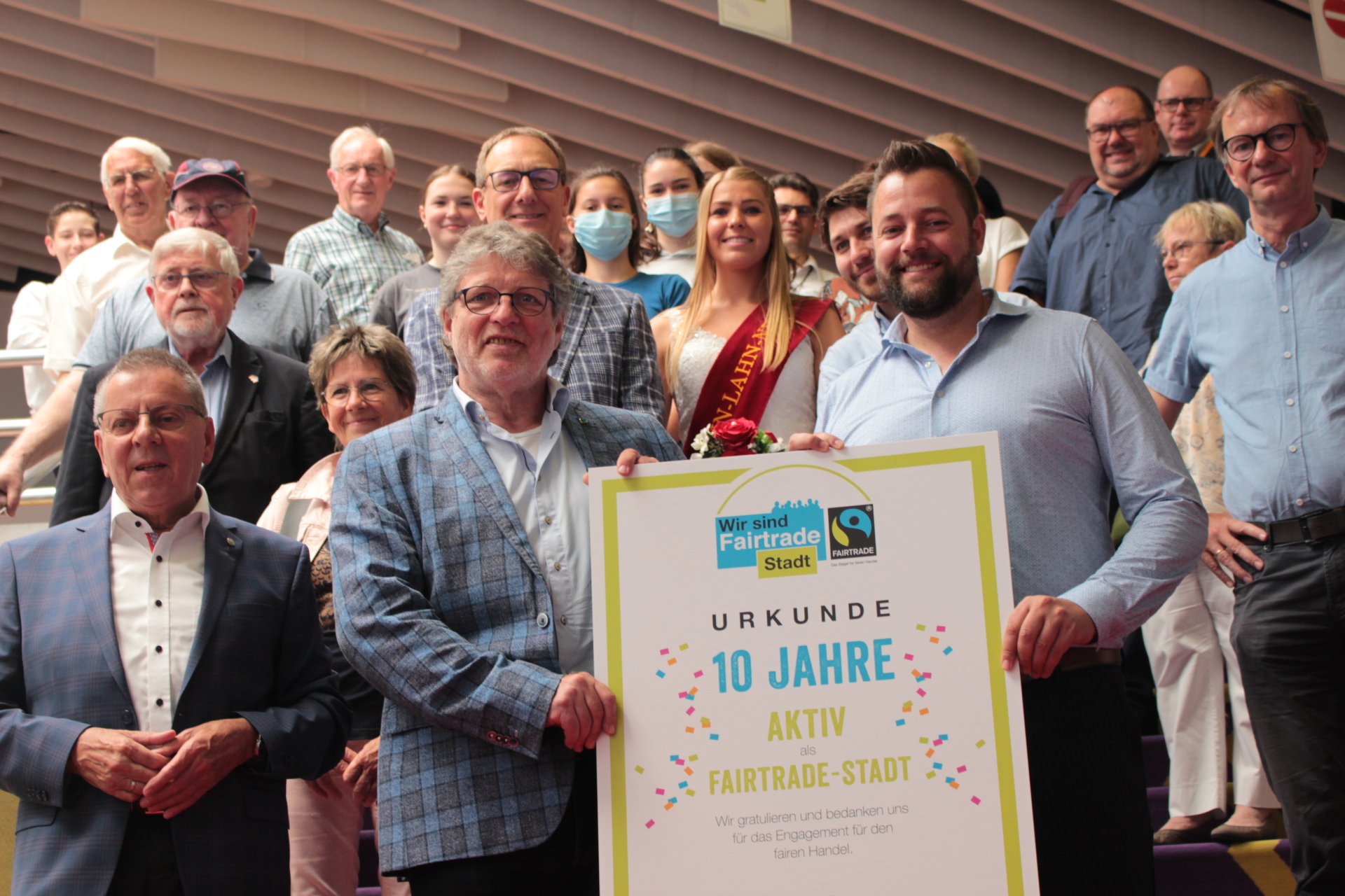 Gruppenfoto mit zahlreichen Mitgliedern der Lahnsteiner Fairtrade-Steuerungsgruppe sowie Unterstützerinnen und Unterstützern. Im Vordergrund halten zwei Männer eine Urkunde zum zehnjährigen Jubiläum der Fairtrade-Stadt Lahnstein.