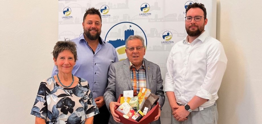 Vier Personen stehen vor einem Roll-up der Stadt Lahnstein. Im Mittelpunkt hält ein Mann einen Präsentkorb mit fair gehandelten Produkten.