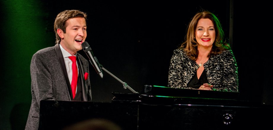 „Die Udo Jürgens Story“ kommt am 11. Januar 2026 nach Lahnstein Alex Parker und Gabriela Benesch stehen vor schwarzem Hintergrund an einem Flügel.