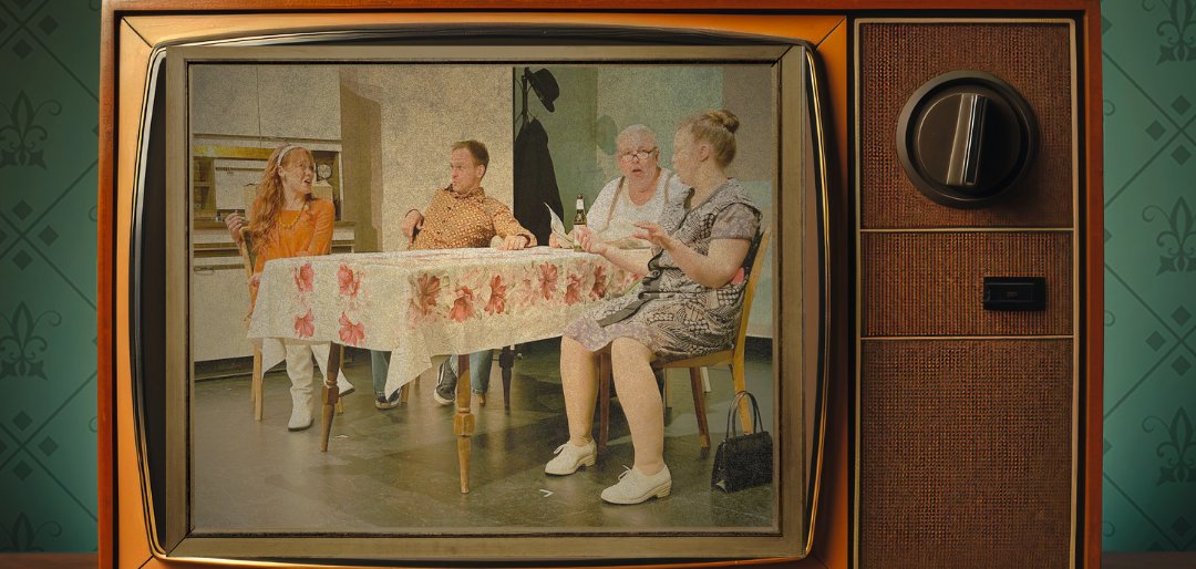 Bildmontage eines alten Röhrenfernsehers auf einem Holzboden vor grün gemusterter Tapete. Auf dem Bildschirm sitzen vier Frauen gemeinsam an einem gedeckten Tisch.