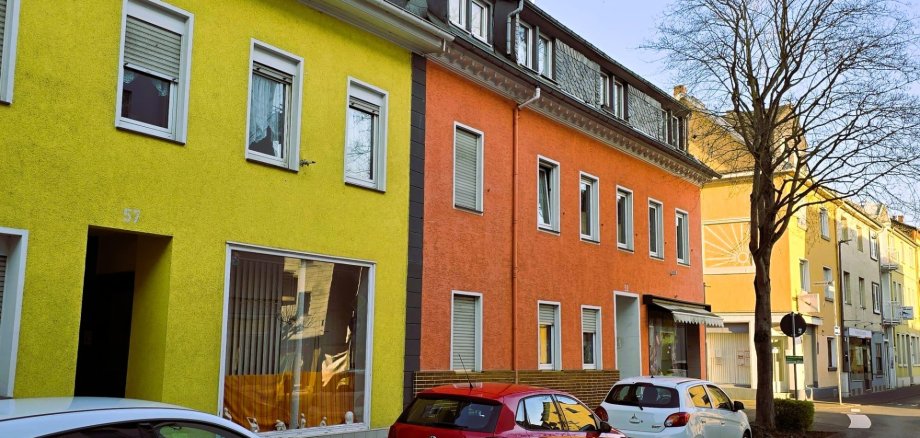 Adolfstraße Lahnstein 2026 Farbfoto einer Straße mit bunt gestrichenen Häusern in Gelb und Orange, parkenden Autos am Straßenrand und einem kahlen Baum im Vordergrund.