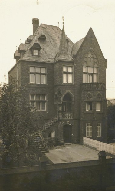 Gebäude in Lahnstein Eine historische Sepia-Fotografie einer imposanten, neugotischen Backsteinvilla in Lahnstein mit steilem Dach, Ziertürmchen und verzierten Fenstern, aufgenommen von einem Innenhof aus.