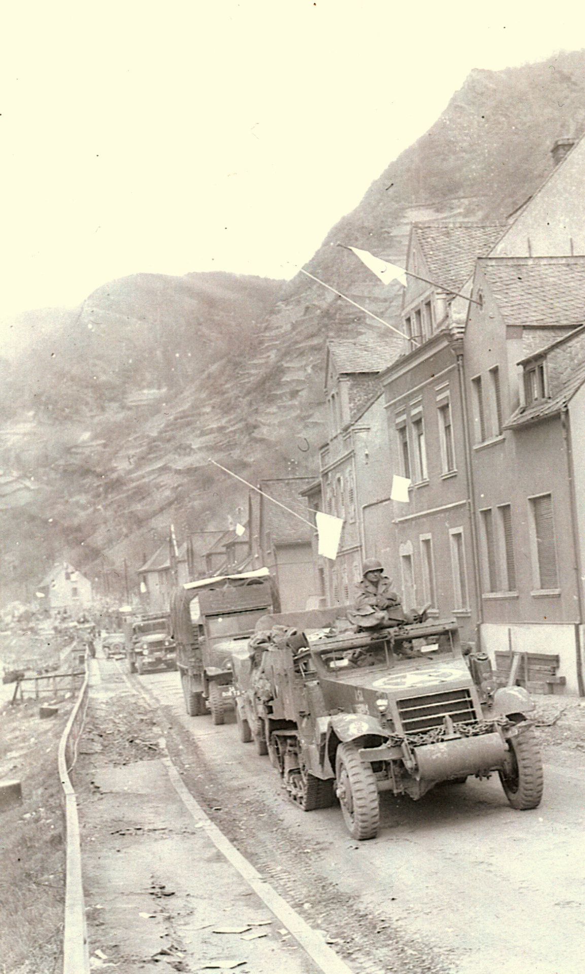 Schwarz-Weiß-Foto von Militärfahrzeugen, die durch eine kaputte Straße fahren.