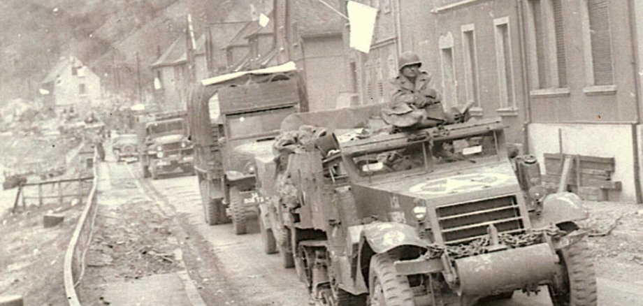 Schwarz-Weiß-Foto von Militärfahrzeugen, die durch eine kaputte Straße fahren.