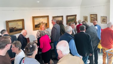 Zahlreiche Besucherinnen und Besucher betrachten dicht gedrängt die ausgestellten Landschaftsgemälde in einem hellen Ausstellungsraum während der Vernissage.