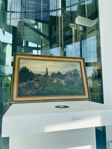 Ölgemälde mit Bauernhofmotiv in goldenem Rahmen steht auf weißem Beton, im Hintergrund ist eine Glasfront zu sehen