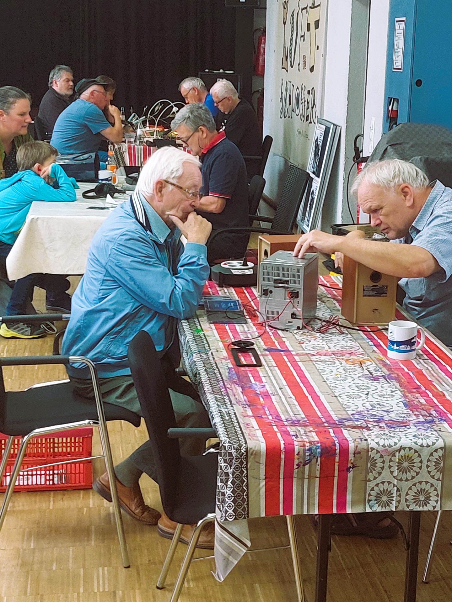Menschen sitzen an einem Tisch und reparieren Elektrogeräte im Repair Café.