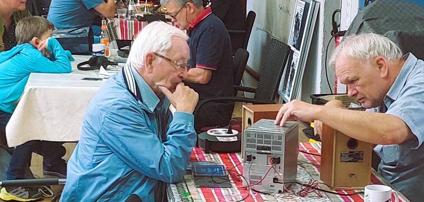 Menschen sitzen an einem Tisch und reparieren Elektrogeräte im Repair Café.