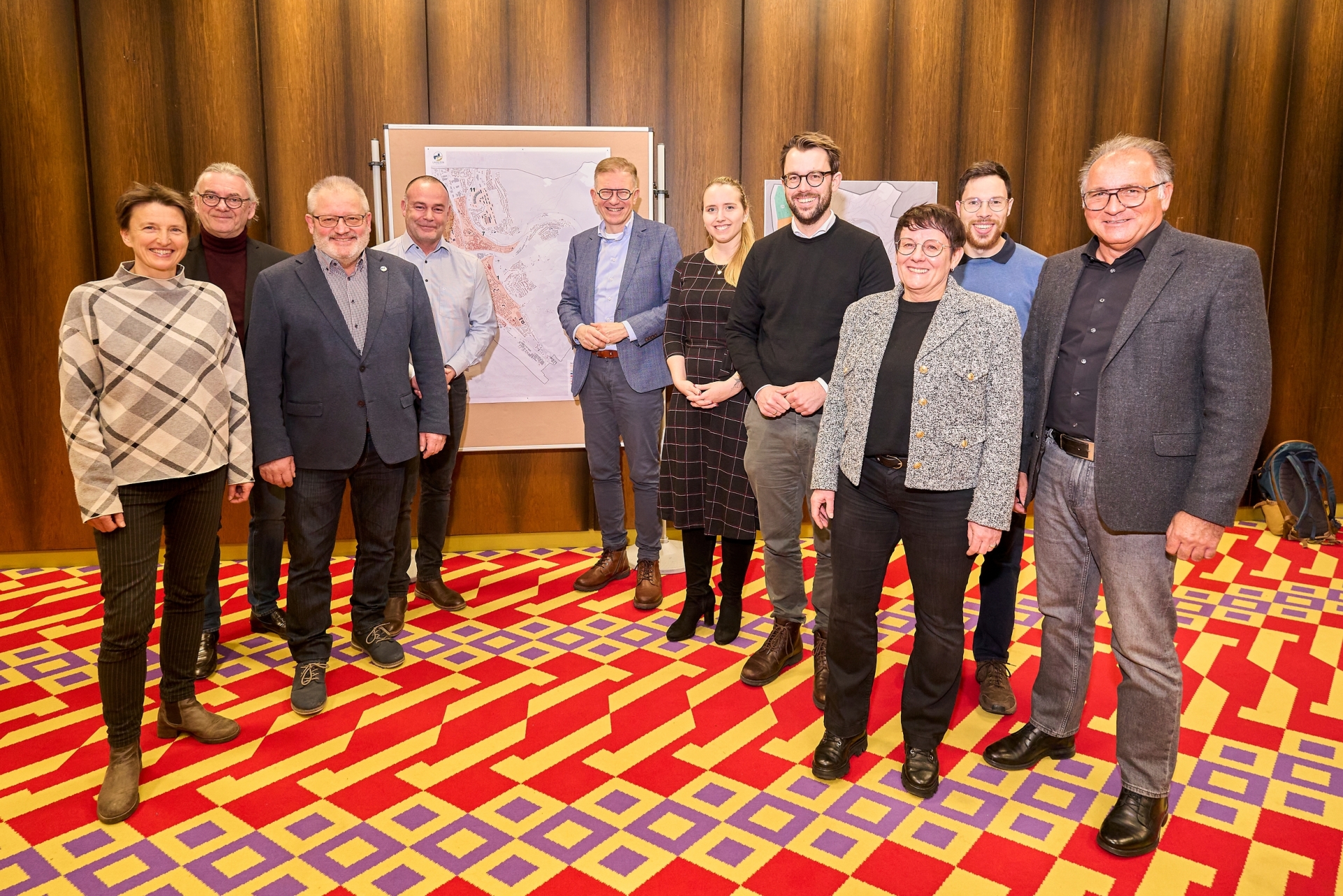 Eine Gruppe von Männern und Frauen steht in der Stadthalle Lahnstein auf dem charakteristischen bunten Teppich vor Schautafeln.