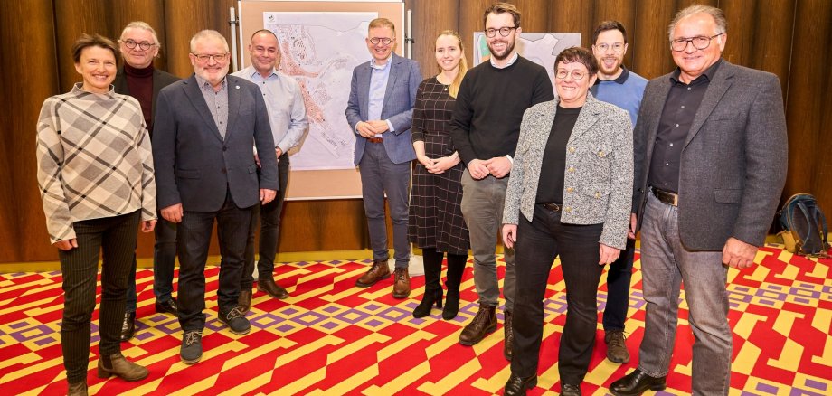 Eine Gruppe von Männern und Frauen steht in der Stadthalle Lahnstein auf dem charakteristischen bunten Teppich vor Schautafeln.