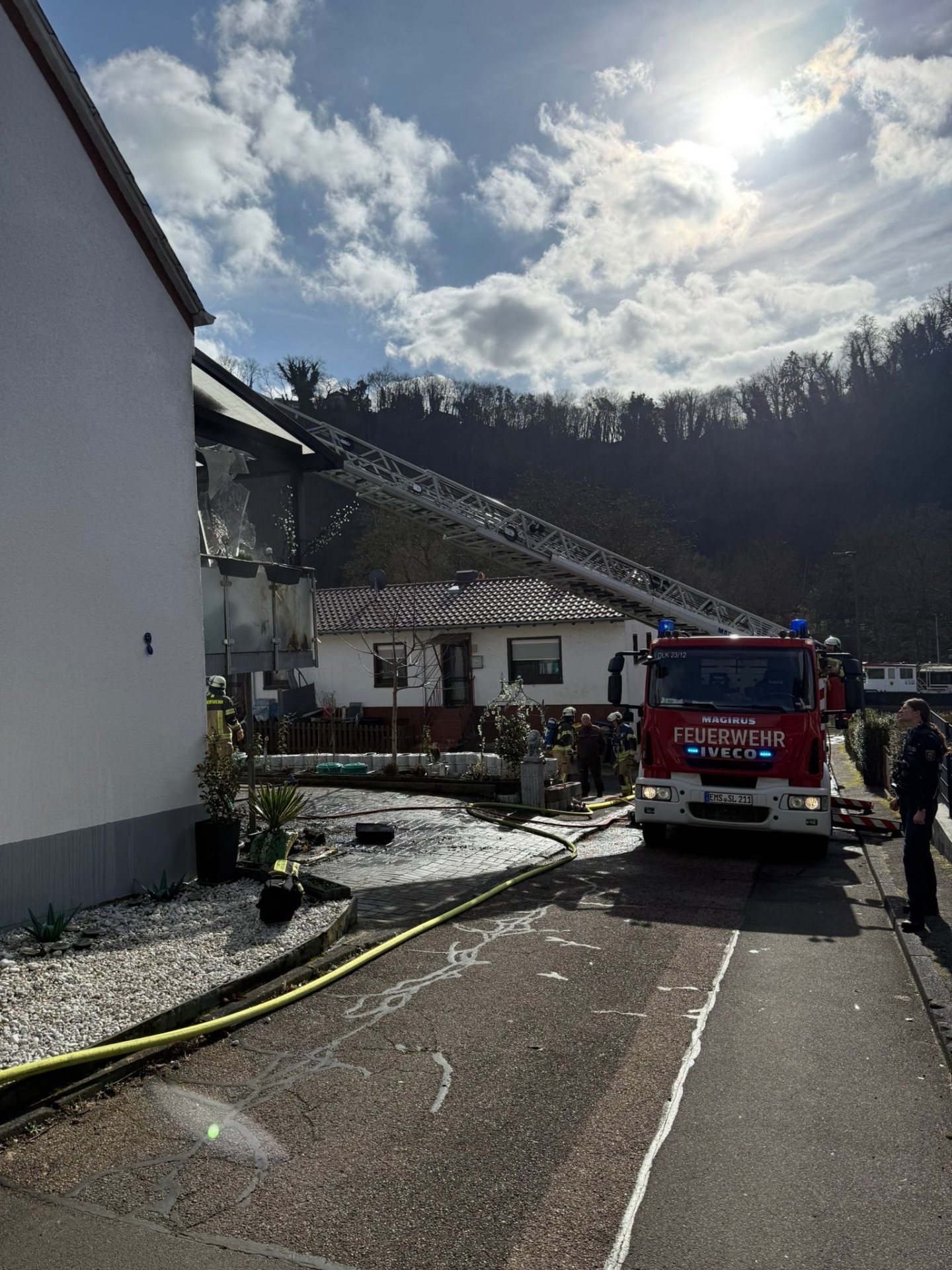 Ein Löschfahrzeug der Freiwilligen Feuerwehr Lahnstein steht mit ausgefahrener Leiter vor dem betroffenen Wohnhaus, der Balkon weist Brandschäden auf. Im Hintergrund sind ein weiteres Haus sowie Einsatzkräfte.
