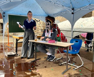 Die Narren regieren in Lahnstein. Eine junge Frau steht vor einer grünen Schultafel. Am Tisch sitzt ein im Gesicht geschminkter Mann, der sich als King Julien aus dem Film Madagaskar verkleidet hat.