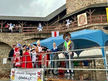 Die Narren erobern Lahnstein Der Karnevalsprinz steht in Tracht zusammen mit seiner Karnevalsprinzessin und seinem Gefolge sowie mehreren kostümierten Menschen auf einer kleinen Bühne. Im Hintergrund ist die dekorierte Stadtmauer erkennbar.
