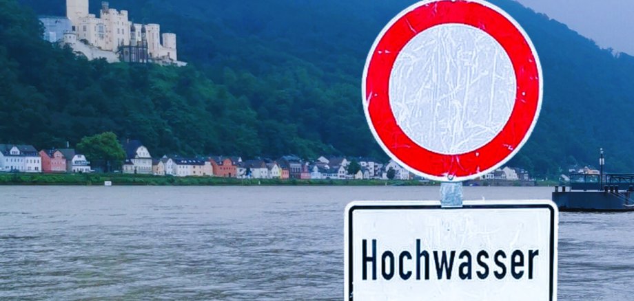 Hochwasser in Lahnstein Im Vordergrund steht ein Durchfahrt-verboten-Schild mit dem Zusatzhinweis "Hochwasser". Im Hintergrund ist ein überschwemmter Berech des Rheinufers Oberlahnstein mit Schloss Stolzenfels zu sehen.
