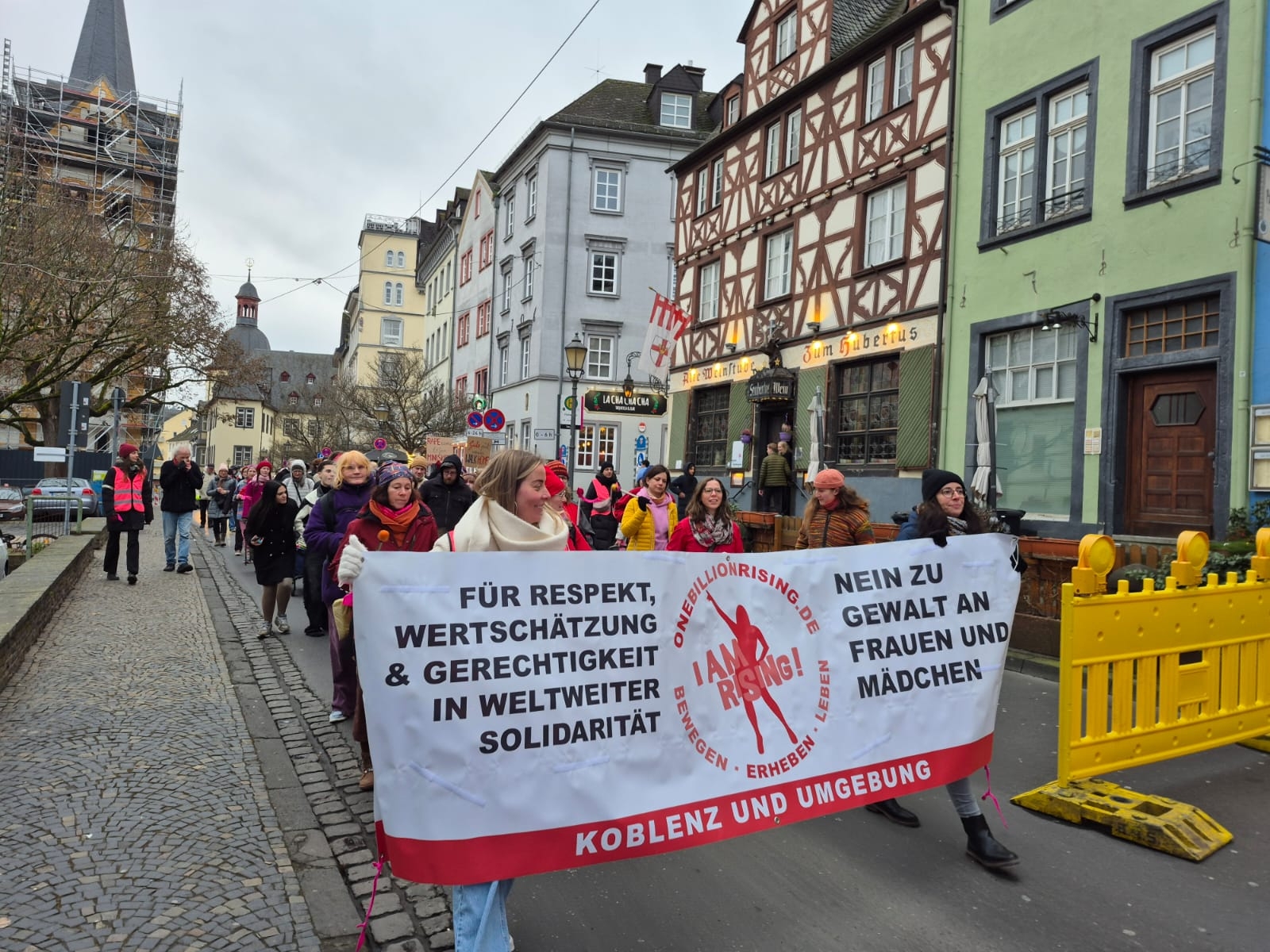 Eine Menge aus überwiegend weiblichen Demonstranten geht gemeinsam auf einer Straße und hält ein Banner hoch, auf dem steht: "Für Respekt, Wertschätzung & Gerechtigkeit in weiltweiter Solidarität" / "Nein zu Gewalt an Frauen und Mädchen"
