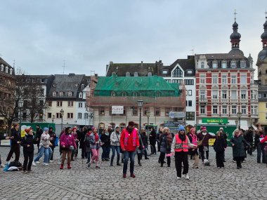 Tanz gegen Gewalt: Auch Lahnsteiner Jugendkulturzentrum setzt Zeichen bei „One Billion Rising“ in Koblenz Eine Gruppe Menschen steht und tanzt auf einem Platz in der Altstadt. Einige von ihnen tragen pinke Warnwesten. Im Hintergrund sind Häuser zu erkennen.