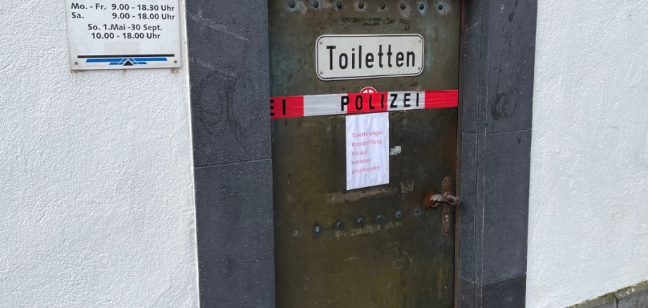 Die Tür zur öffentlichen Toilette mit polizeilichem Absperrband und einem Hinweisschild, dass zurzeit gesperrt ist.