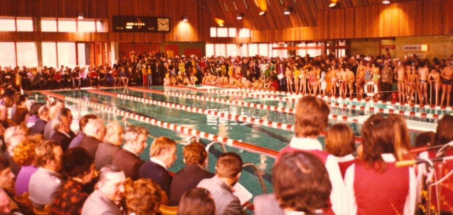 Vor 50 Jahren wurde das Hallenbad eröffnet Anlässlich der Eröffnet befindet sich eine große Menge bekleideter Menschen rund um das Schwimmerbecken im Hallenbad.