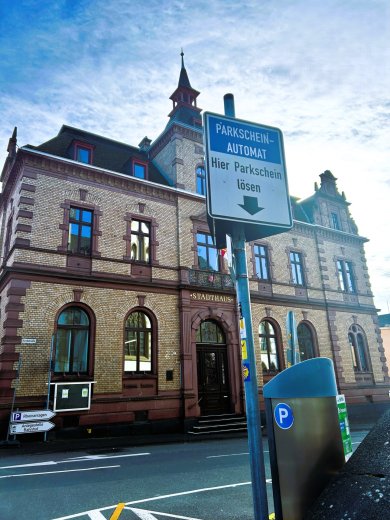 Vor dem städtischen Rathaus ist ein Parkscheinautomat an der Straße mit Hinweisschild zu sehen.