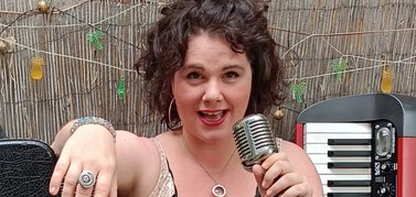 Die Musikerin und Sängerin Sarah Lautermann sitzt mit einem Mikrofon in der Hand neben einem aufgestellten Keyboard.