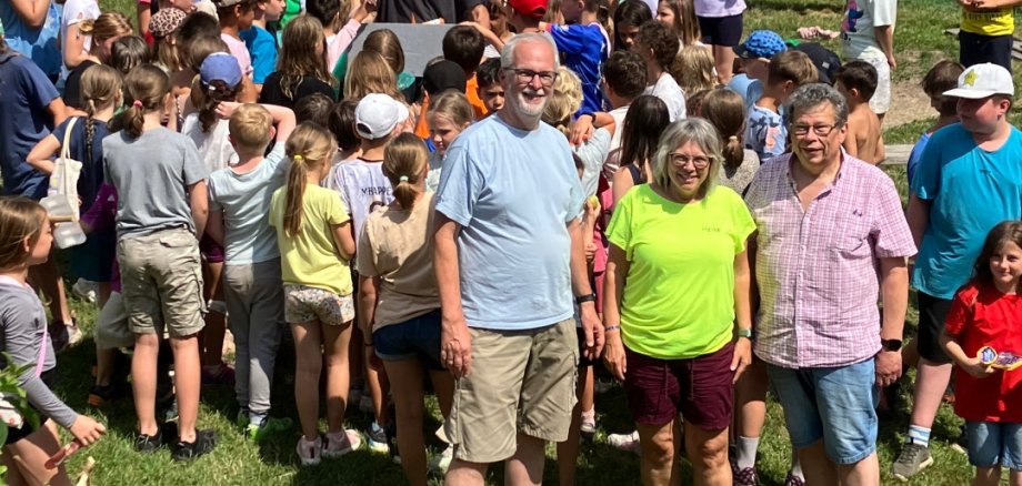 Abwechslungsreiche Ferienangebote für Lahnsteiner Kinder Eine große Gruppe von Kindern versammelt sich auf dem Gelände der AWO-Stadtranderholung. Im Vordergrund stehen Beigeordneter Manfred Radermacher sowie die Leiter Heike und Dirk von Graevenitz. Im Hintergrund sind mehrere weiße Gruppenzelte und spielende Kinder zu sehen.