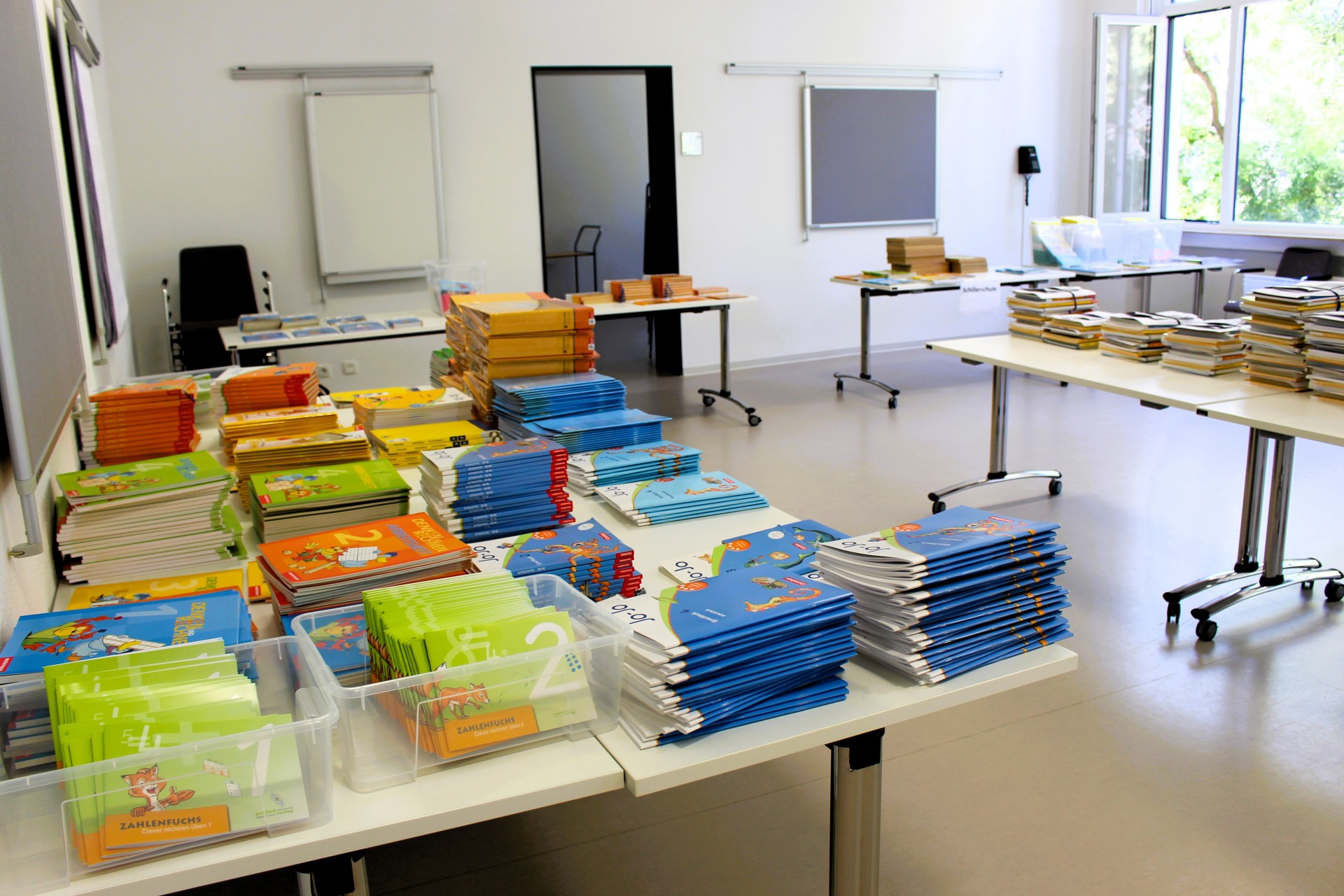 Auf mehrere Tische in einem hellen Raum der Stadtbücherei Lahnstein liegen gestapelte Schulbücher und Lernhefte.