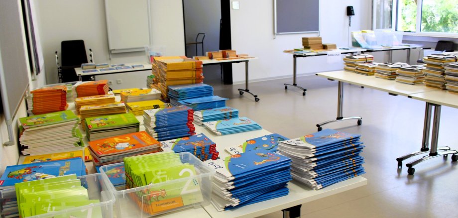 Auf mehrere Tische in einem hellen Raum der Stadtbücherei Lahnstein liegen gestapelte Schulbücher und Lernhefte.