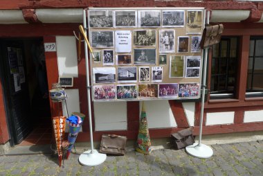 Museumstag Eine Stellwand vor einem Fachwerkhaus zeigt eine Collage aus historischen Schwarz-Weiß- und Farbfotos zum Thema „Mein erster Schultag anno dazumal“, ergänzt durch antike Schultaschen und Zuckertüten am Boden.