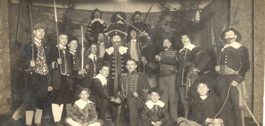 Vom Gesellenverein zur Kolpingfamilie Ein Gruppenfoto einer großen Gemeinschaft vor einer Kirche aus Naturstein. In der Mitte halten Mitglieder ein Banner mit der Aufschrift „Kolping Lahnstein St. Barbara 150 Jahre 1876-2026“, flankiert von zwei Vereinsfahnen.