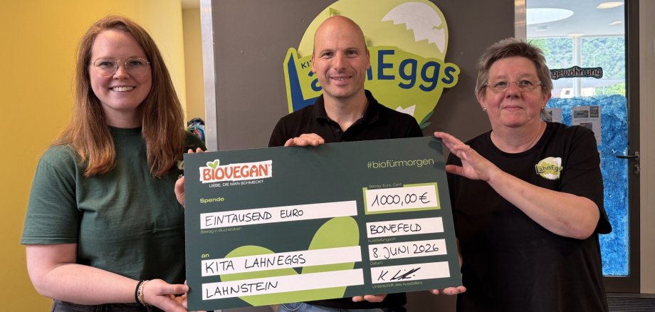 Die kommunale Kita LahnEggs erhält im Rahmen des BIOVEGAN-Projekts „#biofürmorgen“ eine Förderung in Höhe von 1.000 Euro Drei Personen stehen im Eingangsbereich der kommunalen Kita LahnEggs in Lahnstein und präsentieren einen symbolischen Förderscheck über 1.000 Euro aus dem Projekt „#biofürmorgen“ von BIOVEGAN. Im Hintergrund ist das Logo der Kita LahnEggs zu sehen.