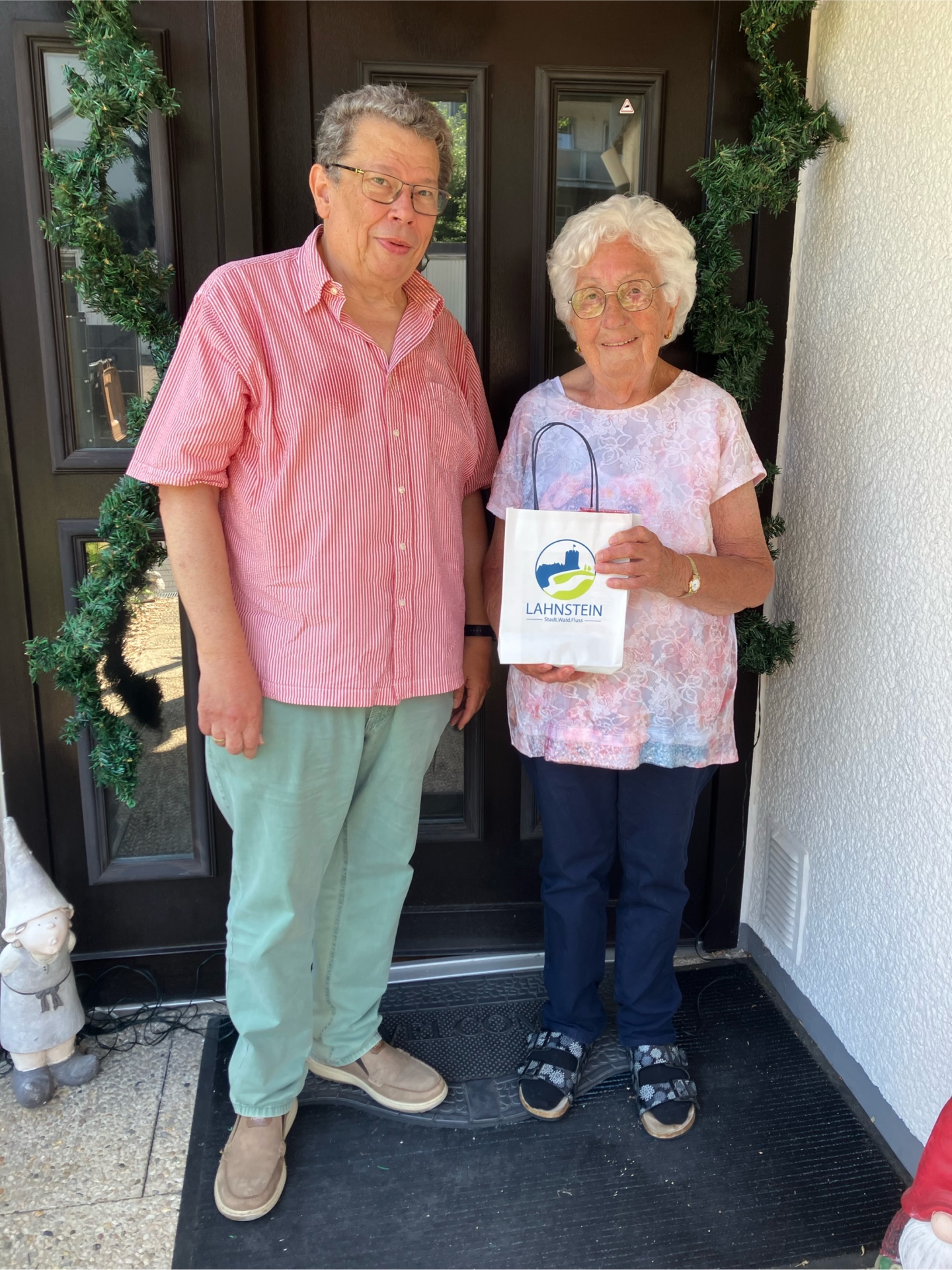Ein Mann und eine Frau stehen zusammen vor einer braunen Tür: Der Beigeordnete Manfred Radermacher gratuliert Elisabeth Heiser zu ihrem 90. Geburtstag. Beide lächeln in die Kamera.