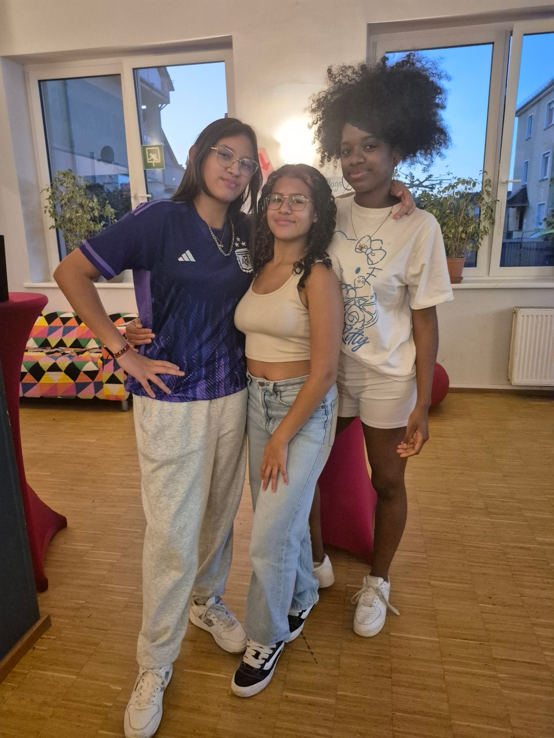 Drei jugendliche Mädchen in sportlicher Kleidung stehen zusammen in einem Raum des Jugendkulturzentrums.