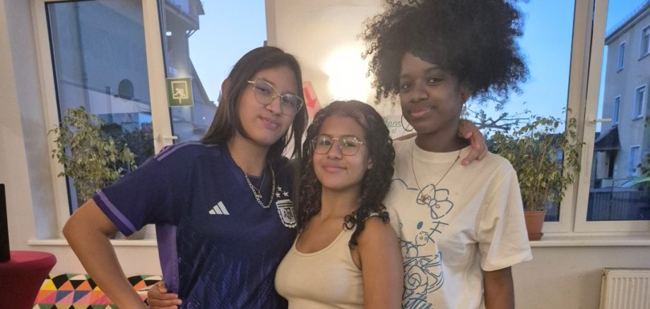 Drei jugendliche Mädchen in sportlicher Kleidung stehen zusammen in einem Raum des Jugendkulturzentrums.