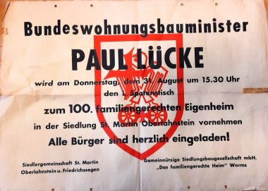 Plakat mit roter und schwarzer Schrift, das den Besuch von Bundeswohnungsbauminister Paul Lücke im Jahr 1961 ankündigt
