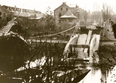 Foto aus dem Jahr 1945 in Sepia, das einen Panzer vor der zerstörten Lahnbrücke in Lahnstein zeigt. Geäst und verschiedene Gebäude sind ebenfalls abgebildet.