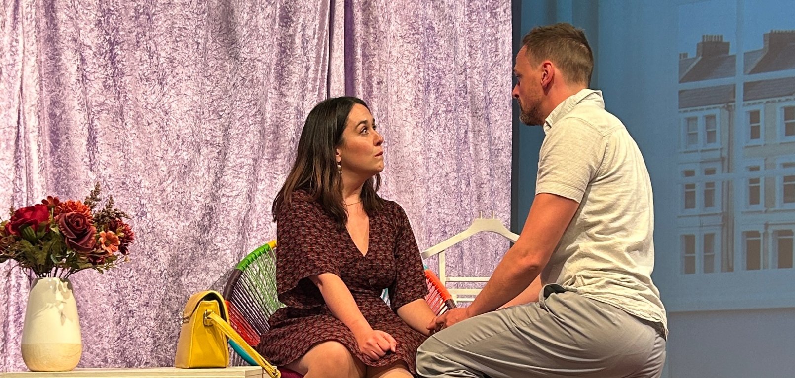 Auf der Bühne des Theater Lahnstein kniet ein Mann vor einer Frau. Auf einem Tisch und auf dem Boden steht jeweils ein Blumenstrauß in einer Vase.