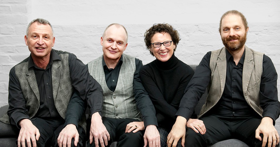 Vier Personen, drei Männer und eine Frau, sitzen nebeneinander in einer Reihe