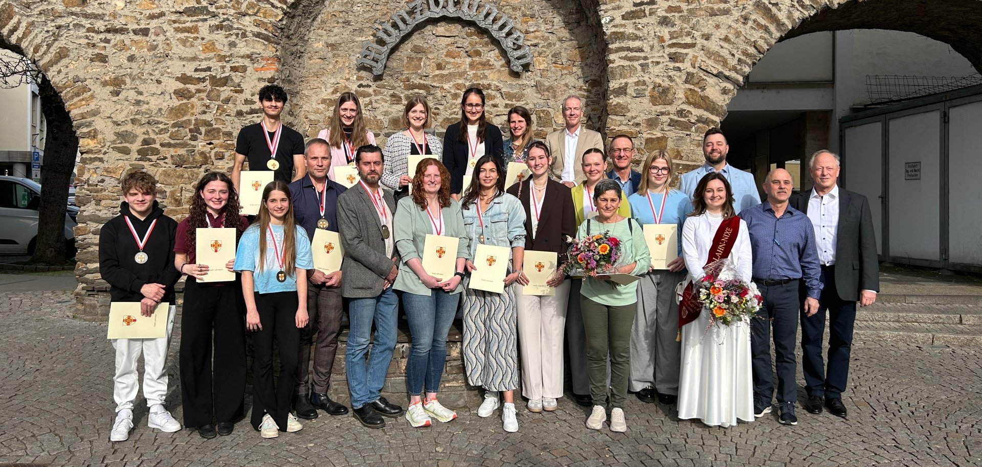 25 Personen stehen in zwei Reihen vor dem Münzbrunnen, einige tragen Medaillen um den Hals und Urkunden in den Händen.