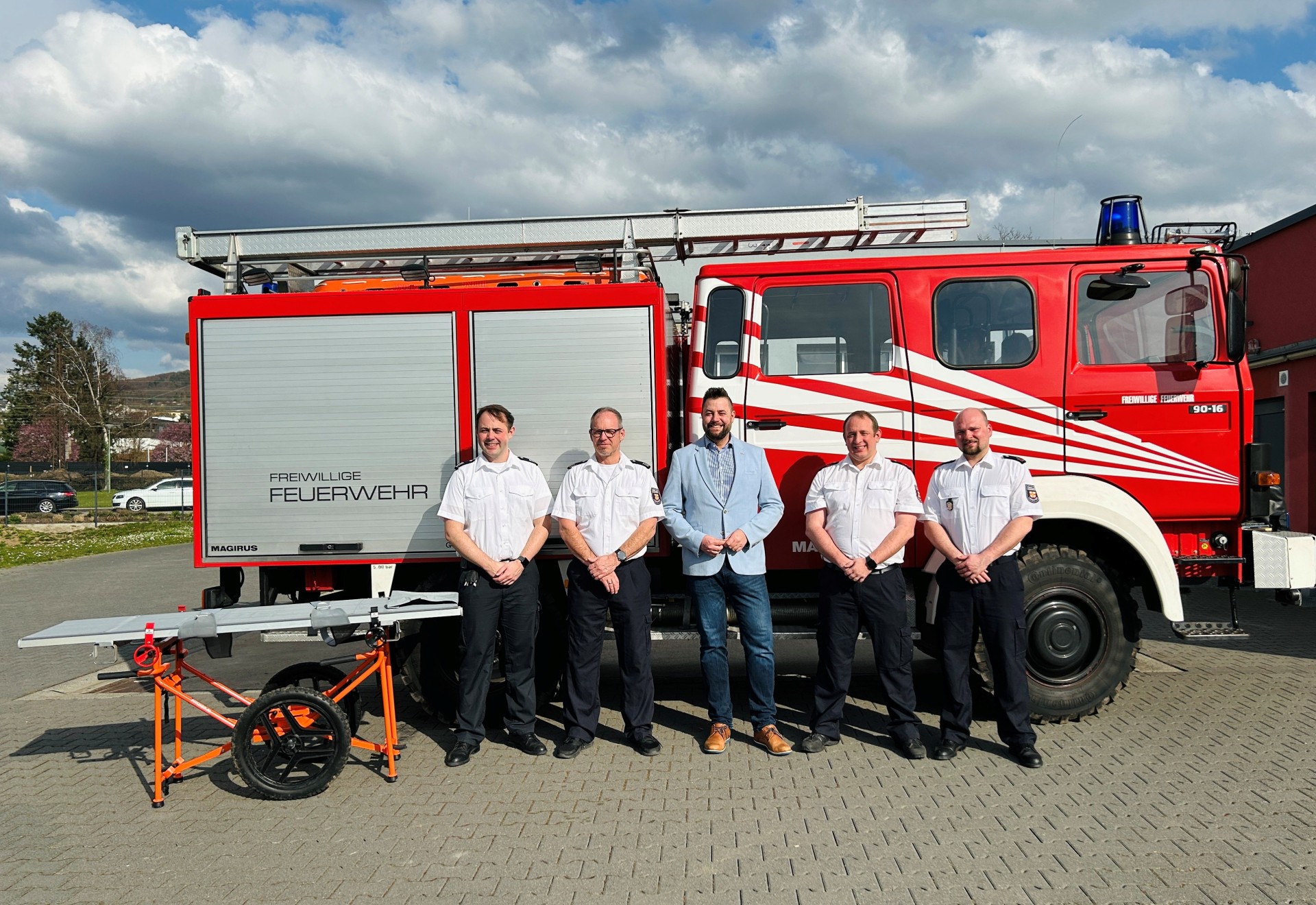 Oberbürgermeister Lennart Siefert steht zusammen mit vier Männern der Freiwilligen Feuerwehr Lahnstein vor einem Löschfahrzeug. Links im Bild ist eine Trage zu sehen.