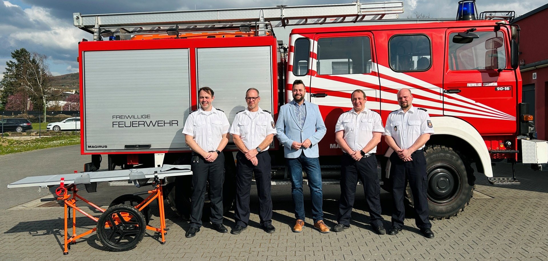 Oberbürgermeister Lennart Siefert steht zusammen mit vier Männern der Freiwilligen Feuerwehr Lahnstein vor einem Löschfahrzeug. Links im Bild ist eine Trage zu sehen.