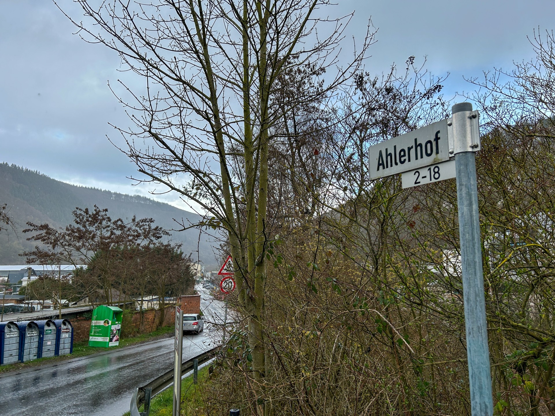 Straße mit Büschen am Rand, im Vordergrund das Straßenschild "Ahlerhof 2-18"