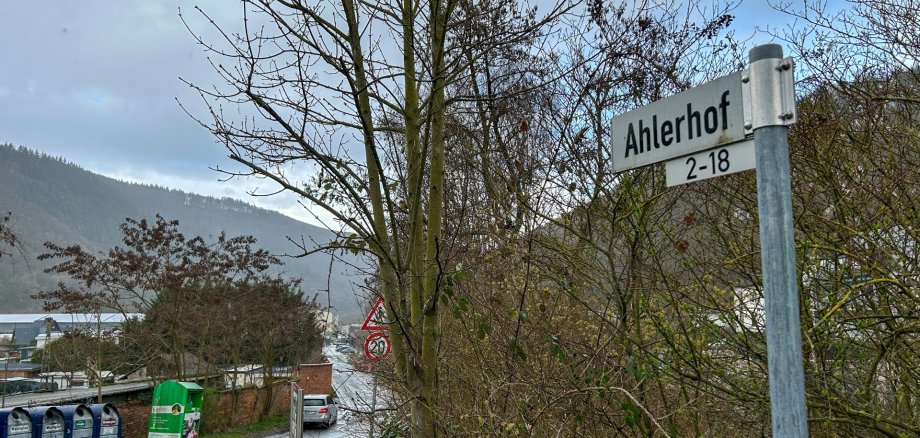Straße mit Büschen am Rand, im Vordergrund das Straßenschild "Ahlerhof 2-18"