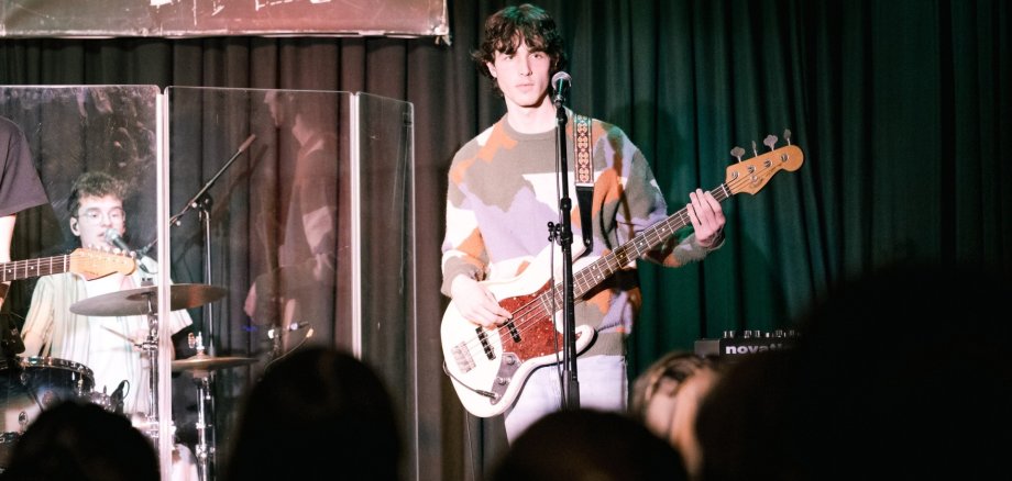 Volles Haus beim Konzert von Herbstwind im Jugendkulturzentrum Ein Musiker spielt E-Bass und singt auf einer Bühne, im Hintergrund Schlagzeuger, im Vordergrund Publikum.